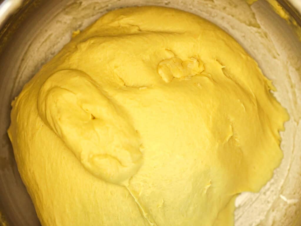 Easy Cherry Brioche Sweet Roll - Vegan Pastry. 24 A close-up of yellow bread dough resting in a metal bowl, ready to rise. The surface appears smooth and slightly glossy.