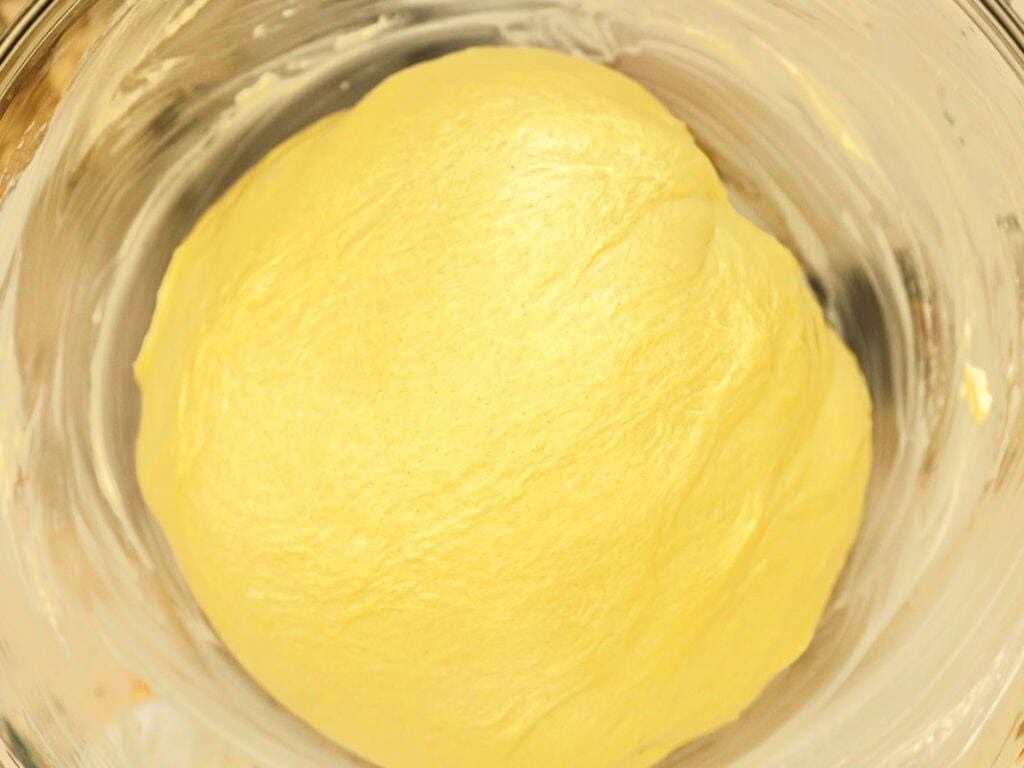 Easy Cherry Brioche Sweet Roll - Vegan Pastry. 25 A close-up of smooth, yellow bread dough resting in a glass bowl, ready to rise. The bowl’s sides are lightly greased, and the dough has a glossy surface.