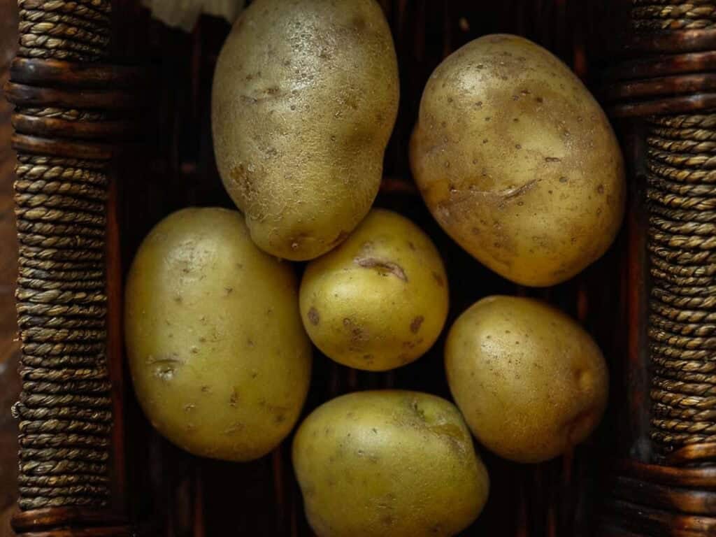 10 Tips for the Perfect Roasted Potatoes Recipe. 3 A close-up of six light brown potatoes with small spots, placed inside a woven basket.