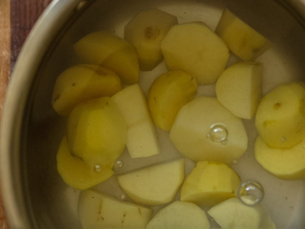 10 Tips for the Perfect Roasted Potatoes Recipe. 6 A pot filled with peeled and chopped potatoes submerged in water, with a few bubbles floating on the surface.