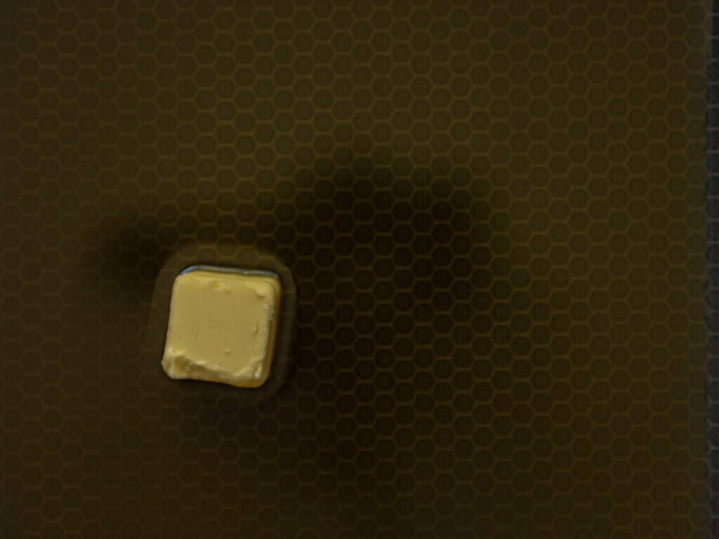 10 Tips for the Perfect Roasted Potatoes Recipe. 14 A small square of butter sits on a brown surface with a faint hexagonal honeycomb pattern.