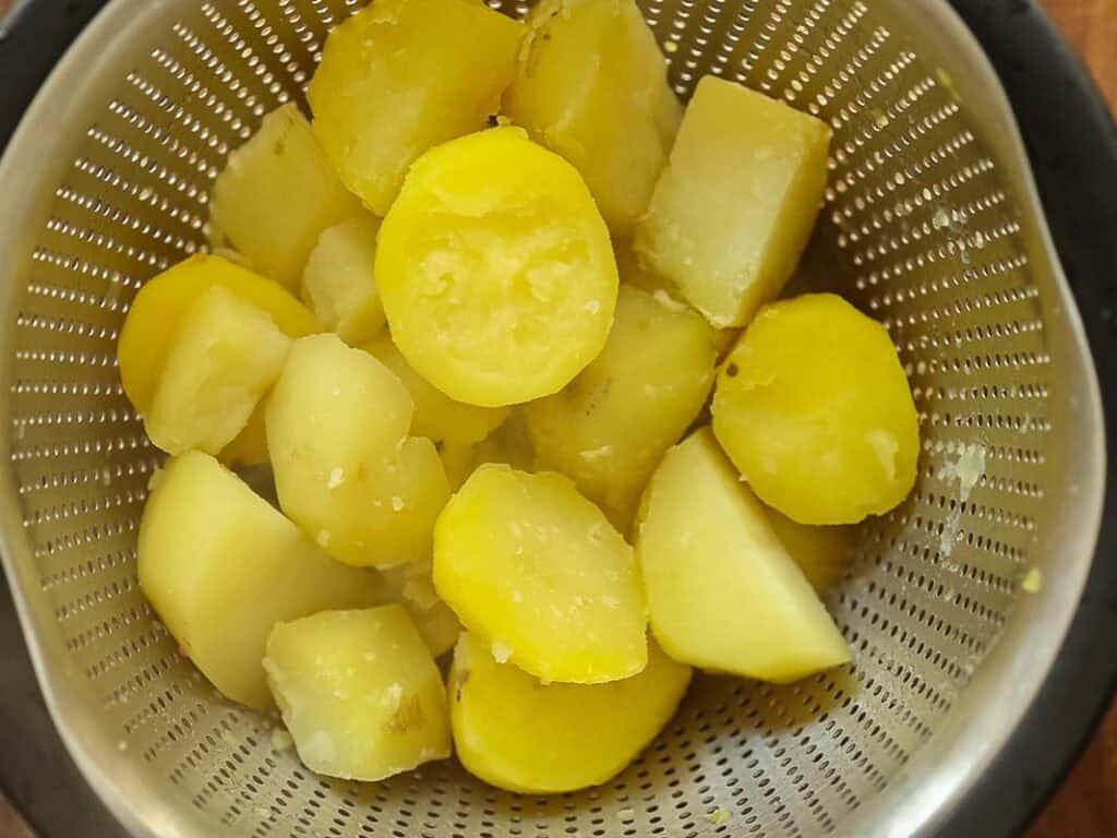 10 Tips for the Perfect Roasted Potatoes Recipe. 18 Boiled, peeled, and chopped yellow potatoes sit in a metal colander, ready to be further prepared or served.