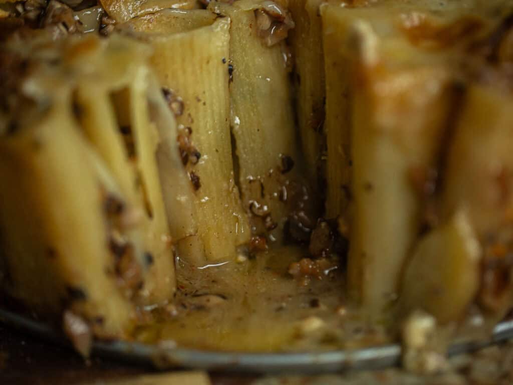 Cheesy Mushroom Rigatoni Pie - Easy Vegan Recipe. 54 Close-up of cooked pasta tubes standing upright, filled with a creamy sauce and chopped mushrooms, with cheese melted on top. The dish appears rich and savory, with a glossy texture and visible seasoning.