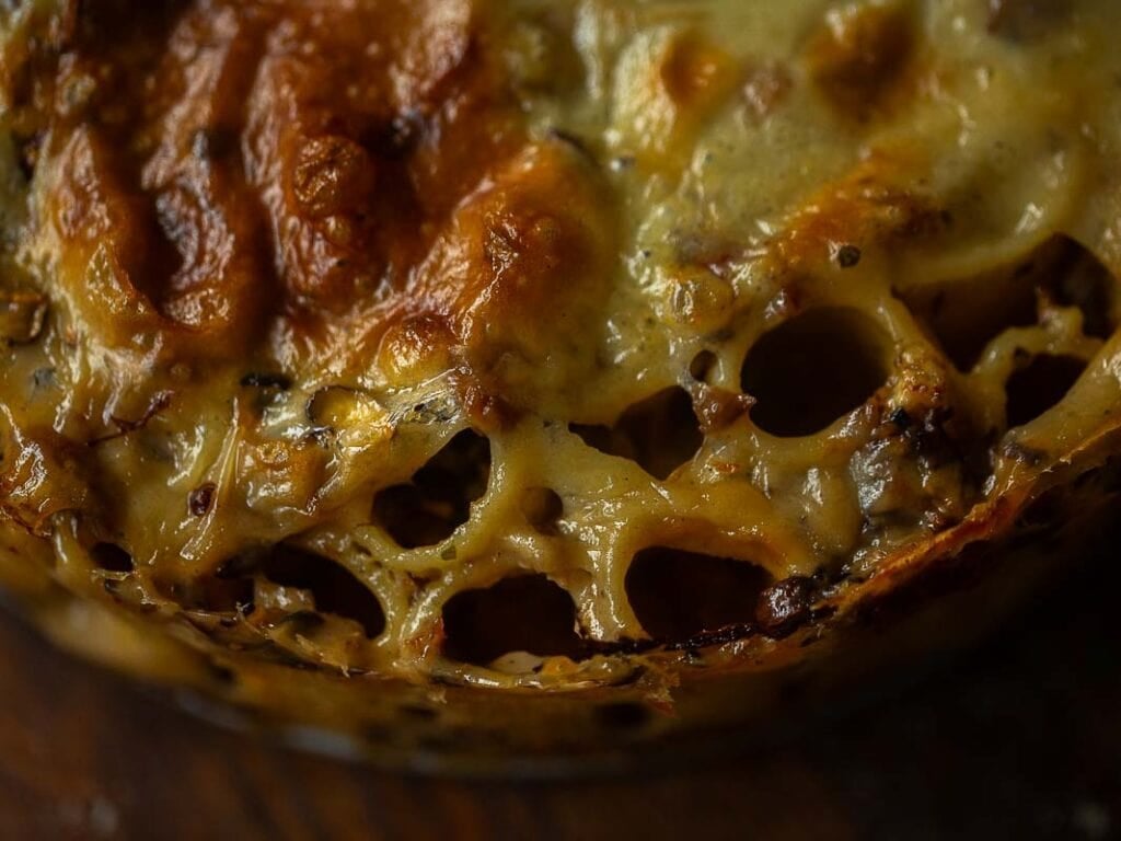 Cheesy Mushroom Rigatoni Pie - Easy Vegan Recipe. 2 Close-up of baked rigatoni pie showing melted, golden-brown cheese and layers of pasta with browned edges, herbs, and bubbly texture.