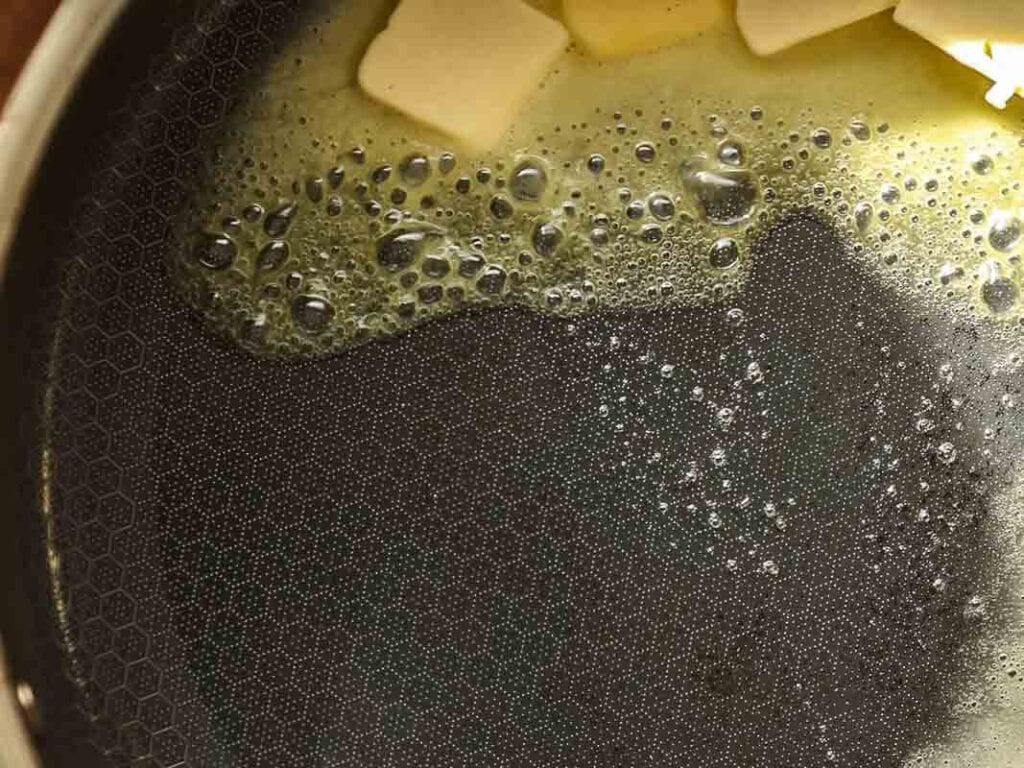 Cheesy Mushroom Rigatoni Pie - Easy Vegan Recipe. 28 Close-up of butter melting in a pan, with small bubbles forming on the surface and several cubes of butter visible at the top edge of the image.