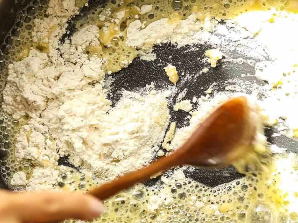 Cheesy Mushroom Rigatoni Pie - Easy Vegan Recipe. 29 A wooden spoon stirs flour into melted butter in a pan, starting the process of making a roux.