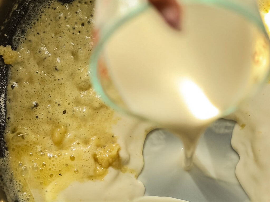 Cheesy Mushroom Rigatoni Pie - Easy Vegan Recipe. 31 Close-up of a creamy liquid, likely milk or cream, being poured into a pan with bubbling melted butter and flour, suggesting the start of making a sauce or roux.