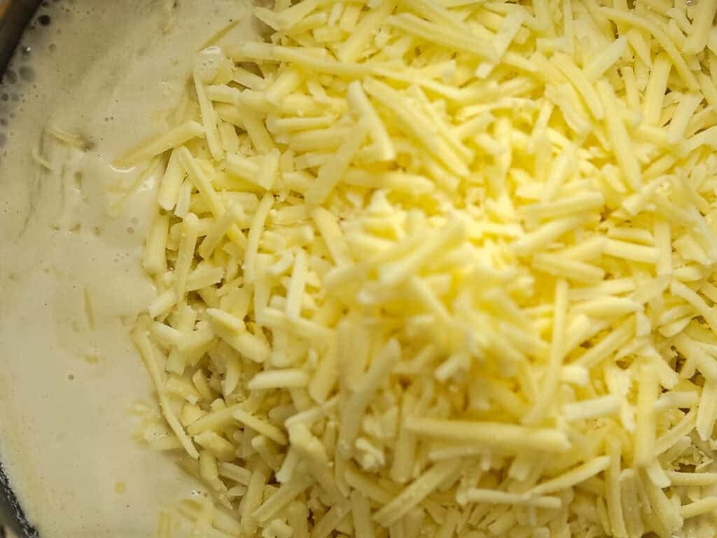 Cheesy Mushroom Rigatoni Pie - Easy Vegan Recipe. 33 A close-up of a pile of shredded cheese on top of a creamy sauce, ready to be mixed together.