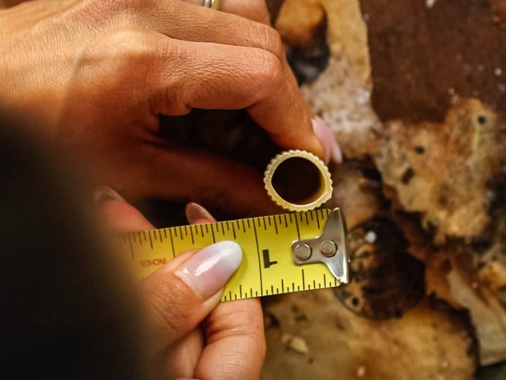 Cheesy Mushroom Rigatoni Pie - Easy Vegan Recipe. 6 A person measures the diameter of a round pasta piece with a yellow tape measure on a rustic, brown surface.