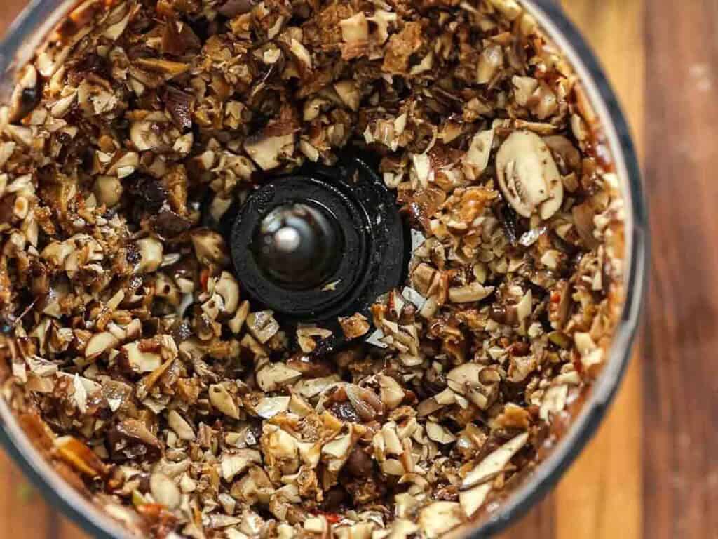 Cheesy Mushroom Rigatoni Pie - Easy Vegan Recipe. 27 Chopped mushrooms and other ingredients inside a food processor, viewed from above, with the blades in the center, ready to be blended further.