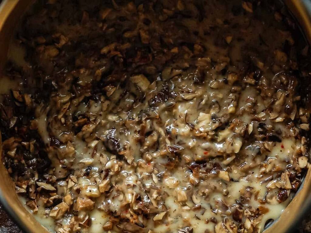 Cheesy Mushroom Rigatoni Pie - Easy Vegan Recipe. 41 A close-up of a creamy mixture with finely chopped mushrooms in a pan, showing a thick consistency and a blend of brown and beige tones.