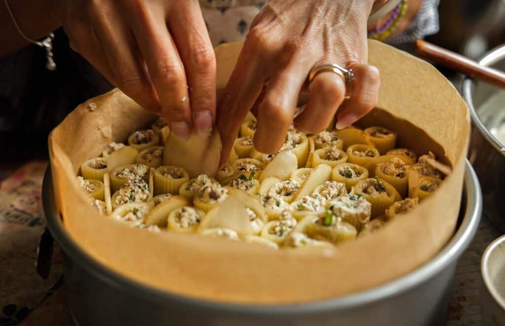 Cheesy Mushroom Rigatoni Pie - Easy Vegan Recipe. 45 someone's hands adding sliced potatoes to rigatoni stuffed with ricotta in a springform pan lined with parchment paper.