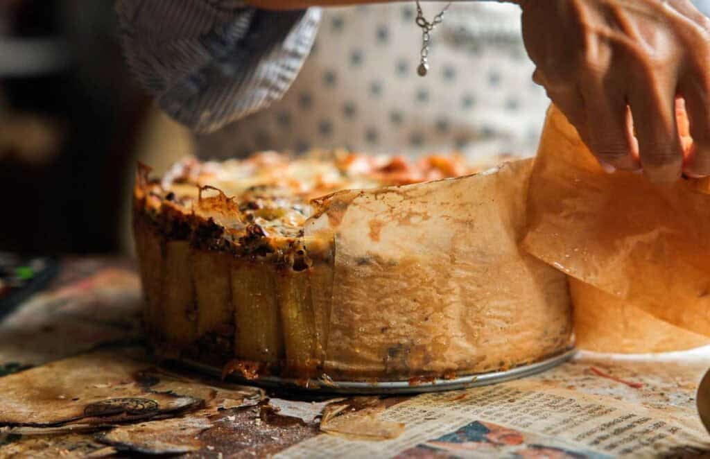 Cheesy Mushroom Rigatoni Pie - Easy Vegan Recipe. 14 someone peeling back the parchment paper off the side of mushroom rigatoni pie.