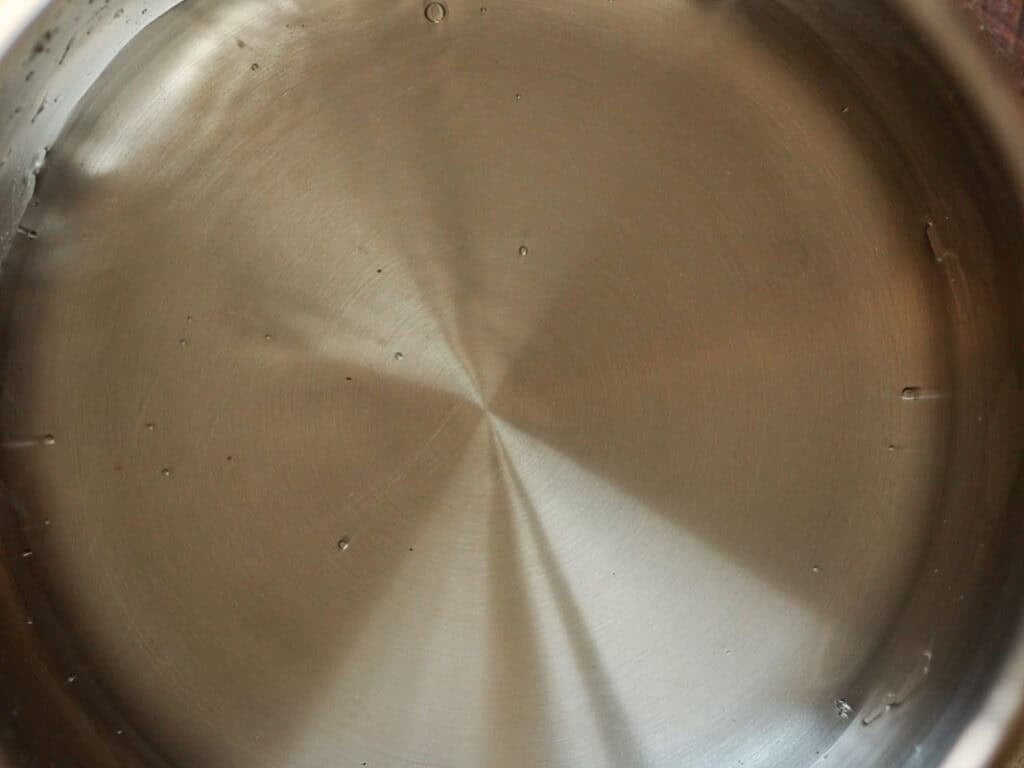 Easy and Delicious Garlic Knots Recipe (Vegan) 4 A close-up view of a stainless steel pot filled with clear water, showing the reflective metal surface and a few small bubbles on the water.
