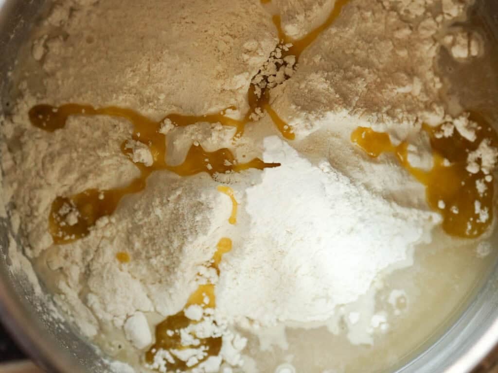 Easy and Delicious Garlic Knots Recipe (Vegan) 6 Close-up of flour and puddles of oil or melted butter in a mixing bowl, with water partially visible around the edges, ready to be mixed into dough or batter.