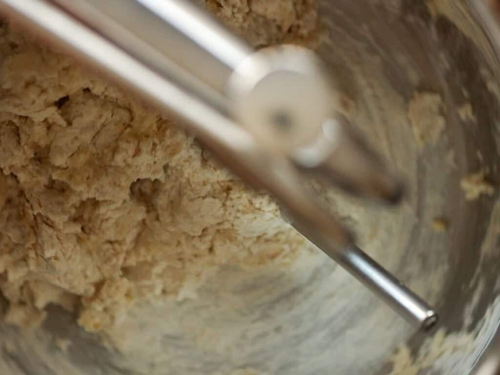 Easy and Delicious Garlic Knots Recipe (Vegan) 7 Close-up of dough being mixed in a metal bowl with a stand mixer, showing the dough hook attachments blending the ingredients.