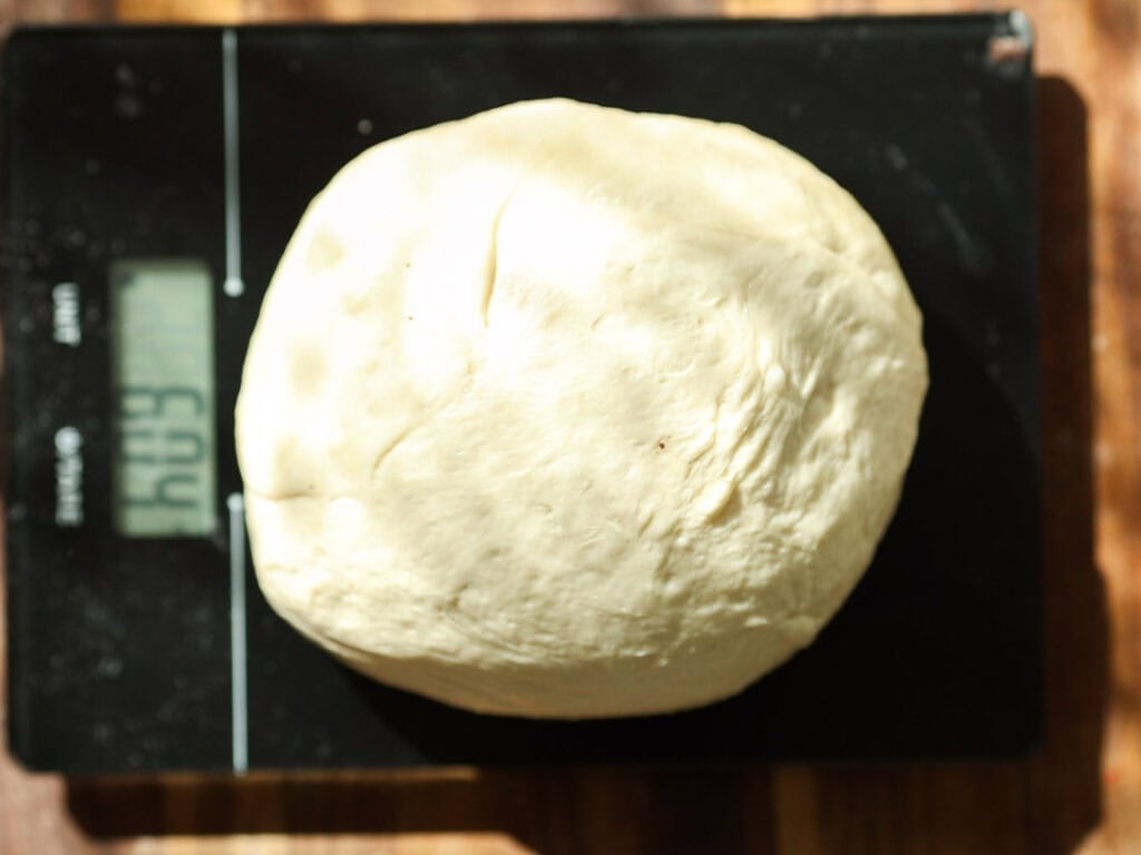 Easy and Delicious Garlic Knots Recipe (Vegan) 11 A ball of dough sits on a digital kitchen scale, which displays a weight of 614 grams. The background is a wooden surface.