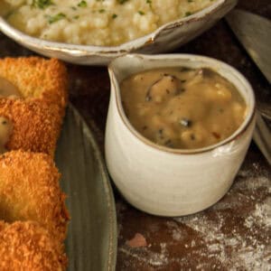 15-minute Quick and Easy Vegan Mushroom Gravy Recipe. 10 A small white ceramic pitcher filled with creamy vegan mushroom gravy sits on a rustic table next to breaded fried food and a bowl of mashed potatoes.