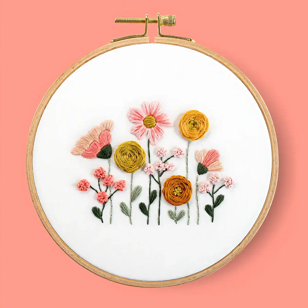 The Korean Vegan's 2025 VEGAN Holiday Gift GUIDE. 43 Embroidery hoop with colorful stitched flowers, including pink daisies and yellow blooms, on white fabric. A perfect vegan holiday gift to brighten any space, set against a solid coral pink background.
