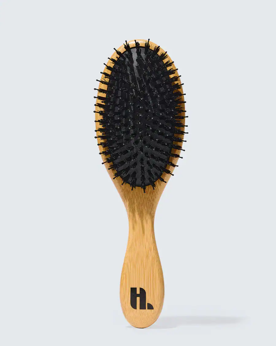 The Korean Vegan's 2025 VEGAN Holiday Gift GUIDE. 32 A wooden hairbrush with black bristles and a light wood handle featuring a stylized H. logo, displayed upright against a plain light gray background—an elegant pick for any Vegan Holiday Gift or Vegan Gift Guide.