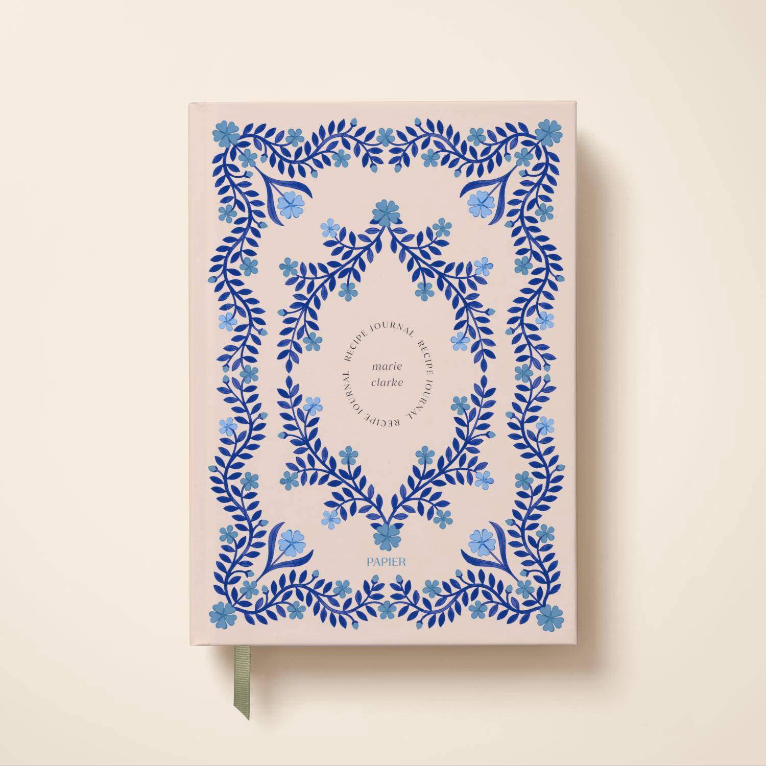 The Korean Vegan's 2025 VEGAN Holiday Gift GUIDE. 24 A light pink journal with blue floral patterns and a green ribbon bookmark, featuring the words Blue Florals Journal by Papier x Marie Claire in the center—an elegant pick for any Vegan Holiday Gift guide.