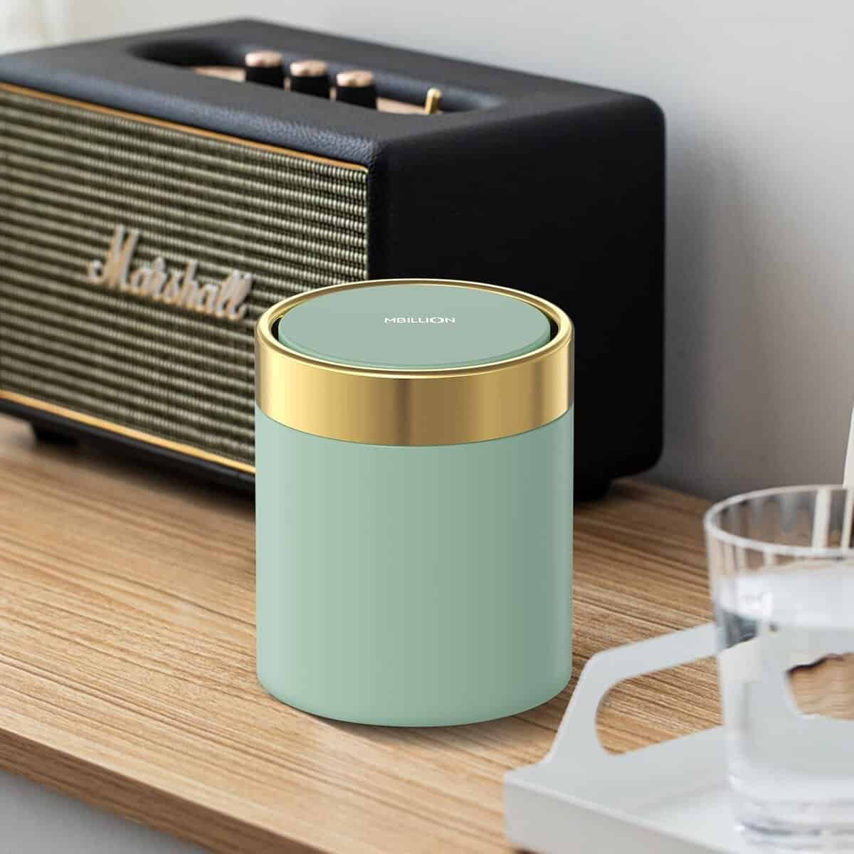 The Korean Vegan's 2025 VEGAN Holiday Gift GUIDE. 26 A mint green container with a gold lid sits on a wooden surface next to a black Marshall speaker. Perfect for any Korean Vegan's 2025 Vegan Holiday Gift Guide, a clear glass of water and part of a white chair are also visible.