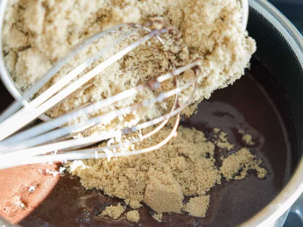 The BEST Vegan Chocolate Cake Recipe On The Internet. 11 A close-up of brown sugar being added to a bowl of chocolate mixture, with a whisk partially submerged in the ingredients.