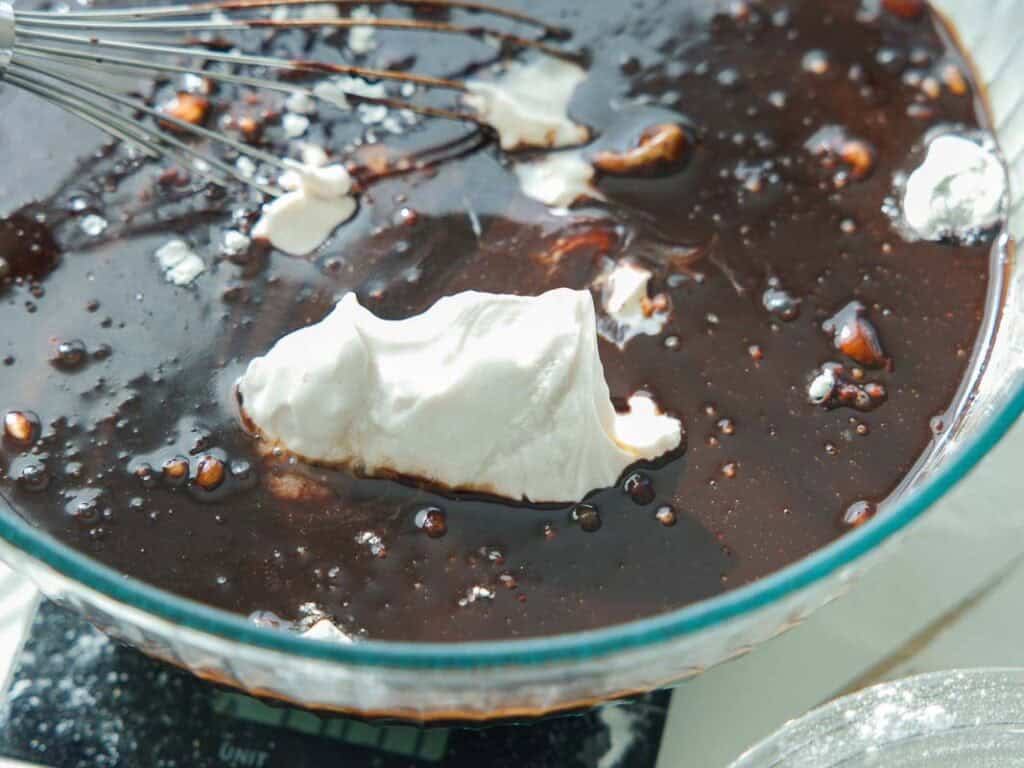 The BEST Vegan Chocolate Cake Recipe On The Internet. 14 A whisk rests in a glass bowl containing a dark chocolate mixture with a large dollop of whipped cream or meringue on top, ready to be mixed together.
