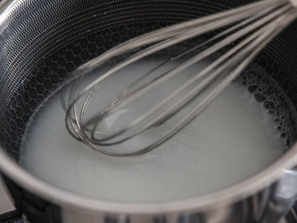 BEST Baby Bok Choy Kimchi Recipe - Easy & Delicious 29 A metal whisk stirs a cloudy slurry in a stainless steel pot with a honeycomb pattern inside, likely on a stoveโprepping pul for Vegan Ponytail Kimchi, an essential step in a Chonggak-Kimchi recipe.
