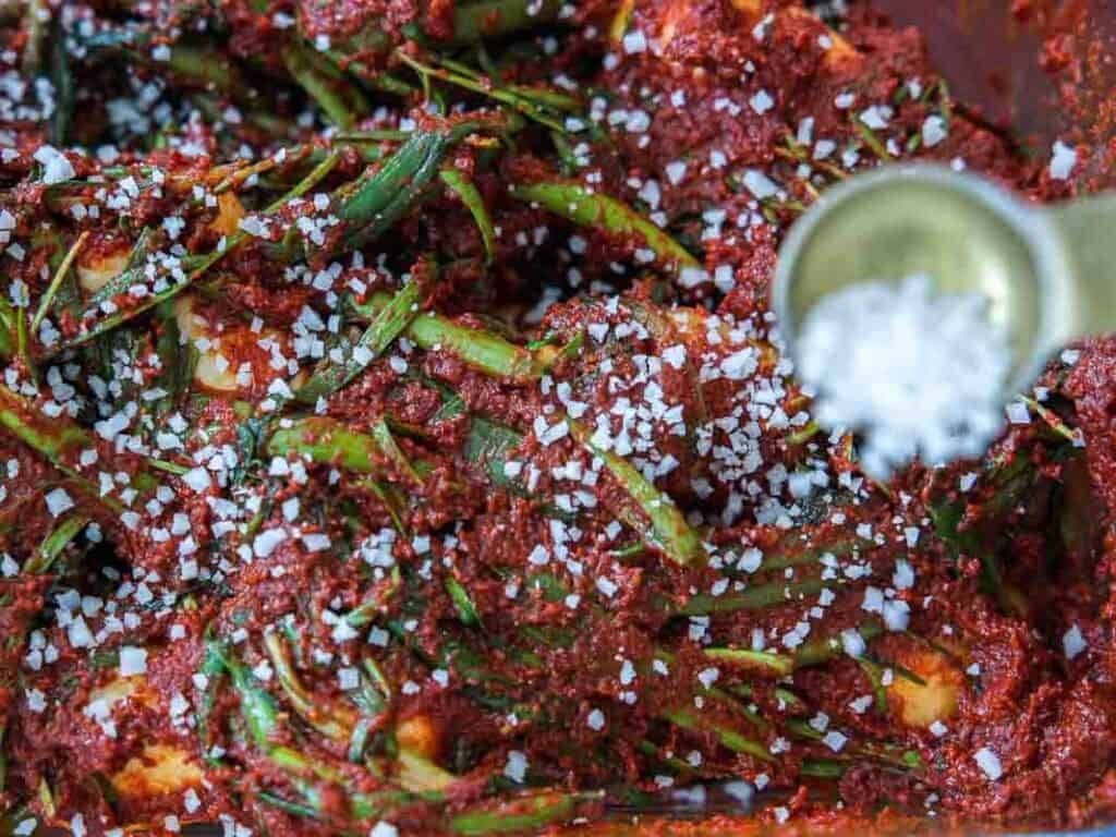 Vegan Ponytail Kimchi aka Chonggak-Kimchi Recipe. 48 A close-up of Vegan Kimchi being prepared, with green onions, red chili paste, and coarse salt sprinkled on top—capturing the vibrant process of making traditional Ponytail Kimchi.