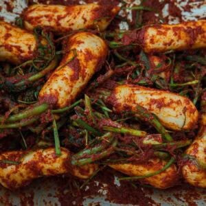 Vegan Ponytail Kimchi aka Chonggak-Kimchi Recipe. 51 Close-up of Vegan Ponytail Kimchi, showing white radishes coated in red chili paste with green onions and seasoning mixed throughout—an authentic Vegan Kimchi twist on the classic Chonggak-Kimchi recipe.