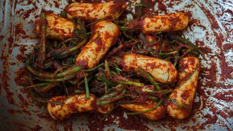 Big bowl of ponytail kimchi: korean baby radishes coated in red chili paste are mixed with green herbs and spices in a metal bowl, illustrating the ingredients for a classic Vegan Kimchi or an authentic Chonggak-Kimchi Recipe.