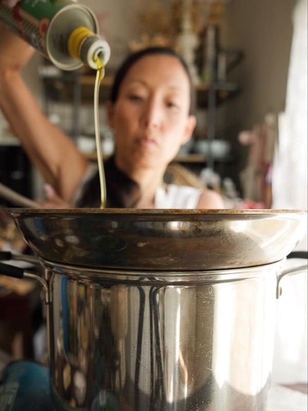 8-ingredient Easy and Delicious Lemon Pepper Pasta. 6 A person pours olive oil into a large metal pot on the stove, preparing to cook Easy Pasta in the kitchen. The focus is on the oil and pot, with the person blurred in the background.