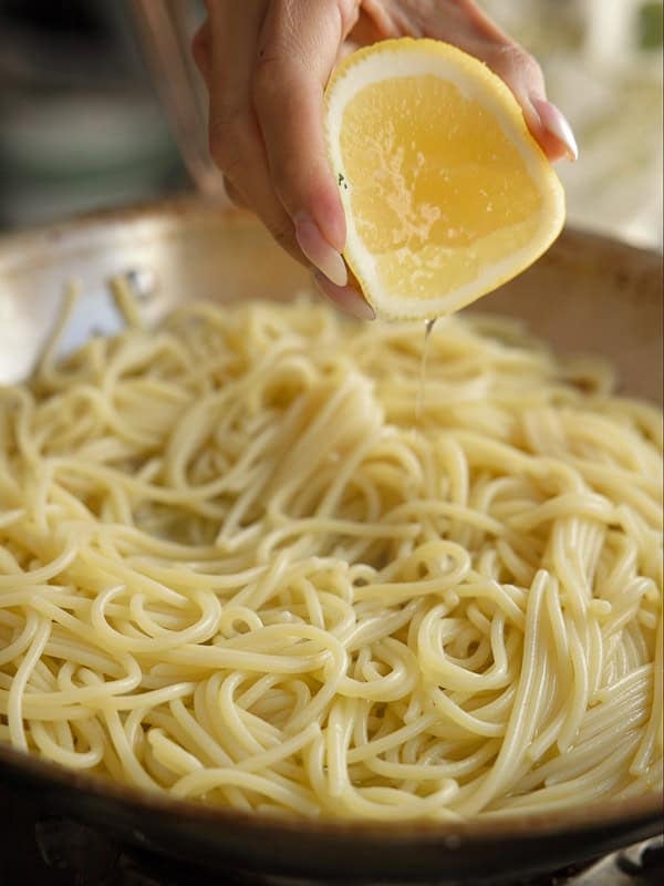 8-ingredient Easy and Delicious Lemon Pepper Pasta. 13 A hand squeezes a lemon wedge over a pan of cooked spaghetti noodles, with fresh juice dripping onto the pasta—perfect for creating flavorful Lemon Pepper Pasta.
