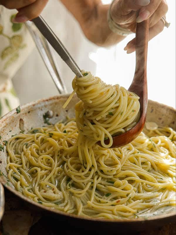 8-ingredient Easy and Delicious Lemon Pepper Pasta. 17 A person uses tongs and a wooden spoon to lift a serving of delicious pasta with herbs and sauce from a pan.