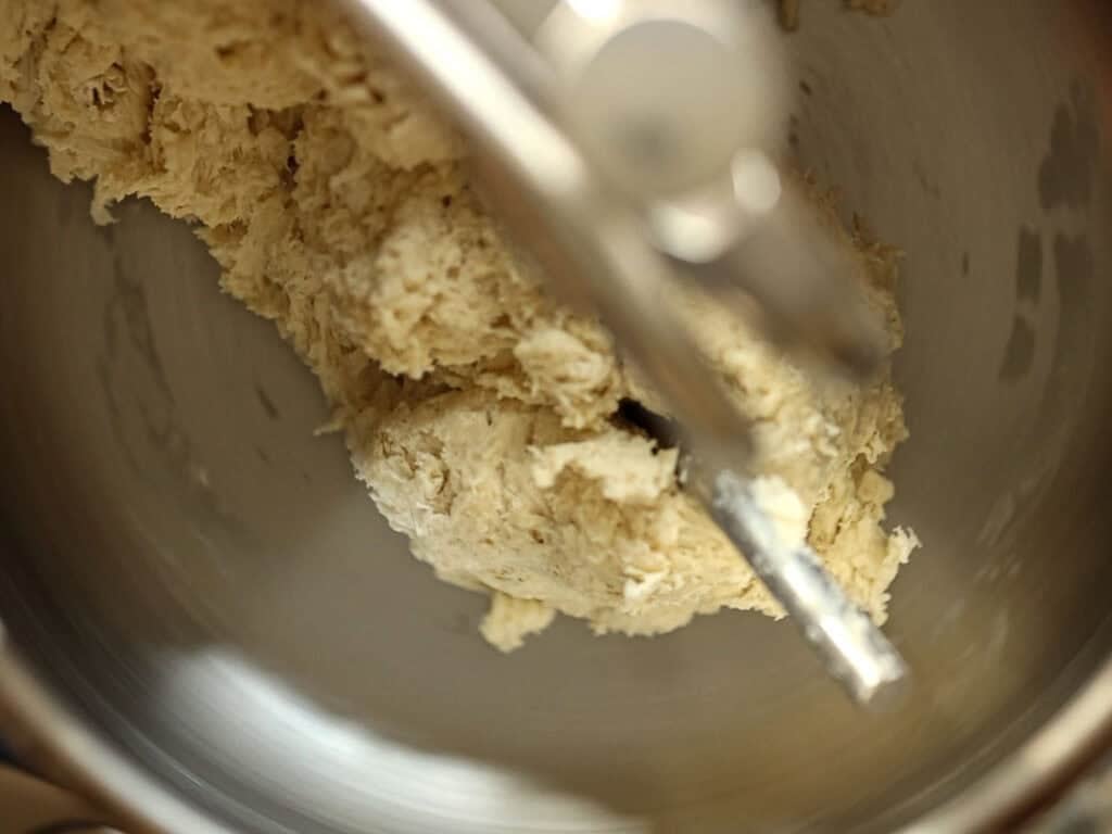 How to Make Viral Salt Bread Recipe (Easy and Vegan). 11 A close-up of vegan bread dough being mixed in a metal stand mixer bowl, with the dough hook attachment visible—perfect for your next viral salt bread recipe.