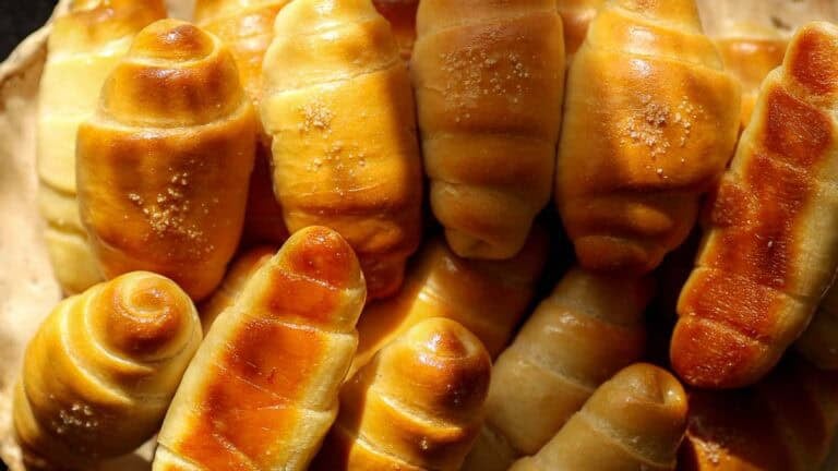 A close-up view of freshly baked, golden brown vegan salt bread rolls with a shiny, glazed surface and a sprinkle of sugar on top, arranged closely together—a perfect easy salt bread recipe.