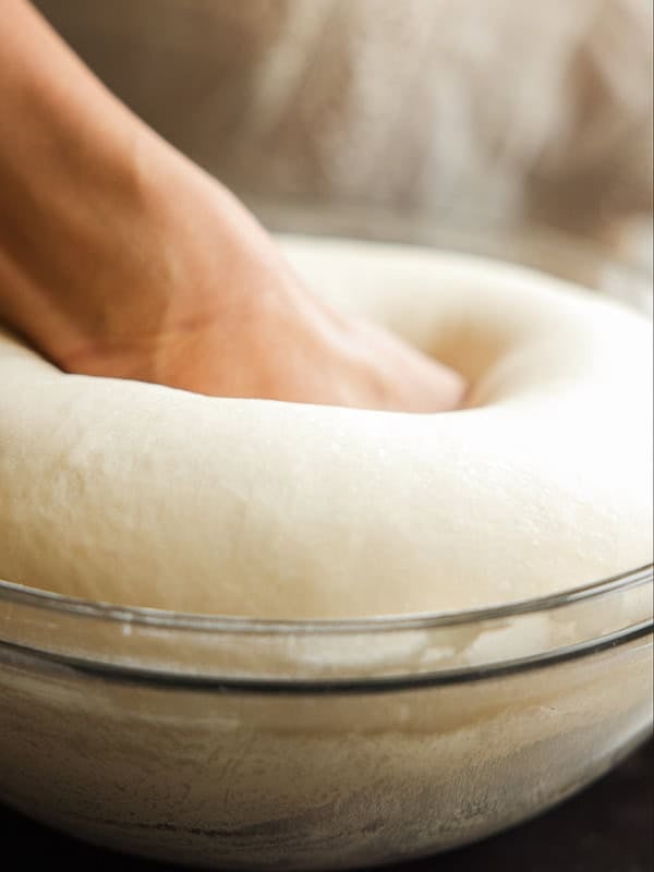 How to Make Viral Salt Bread Recipe (Easy and Vegan). 17 A hand presses down into a risen ball of dough in a glass bowl, showing the dough’s soft and fluffy texture—perfect for trying that viral bread or your favorite vegan bread recipes.