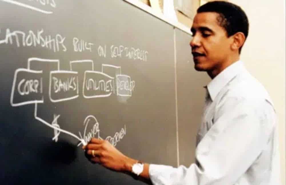 That time I met Barack Obama. 1 A man in a white shirt writes and draws diagrams with rectangles and text on a blackboard in a classroom setting, discussing topics like CORP, BANKS, UTILITIES, and RELATIONSHIPS BUILT ON SELF-INTEREST.