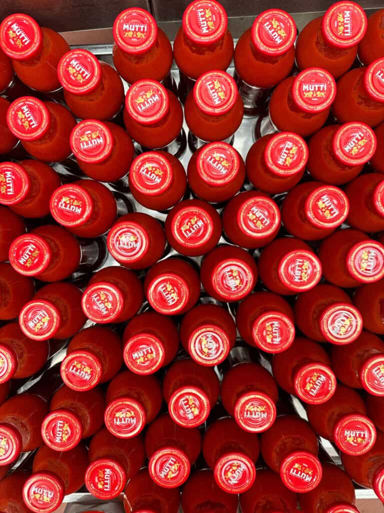 Da Vinci & Mutti: A Visit to Parma, Italy. 17 Rows of red-capped Mutti tomato sauce bottles, a taste of Parma, Italy, are closely arranged and viewed from above, each cap clearly displaying the brand name and logo.