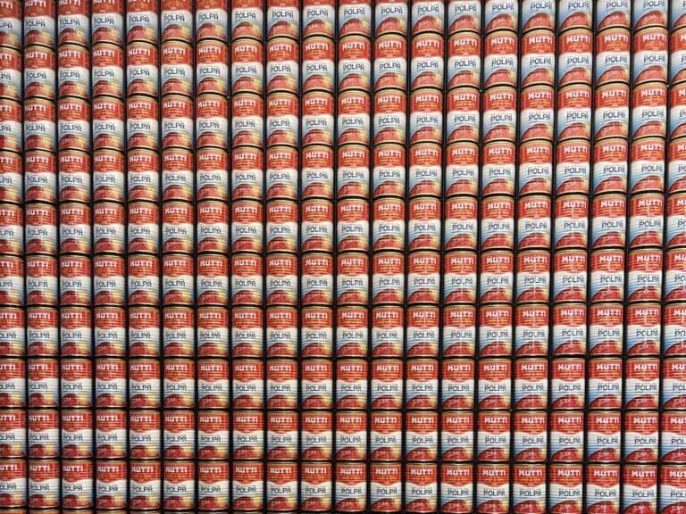 Rows of Mutti Polpa finely chopped tomatoes cans are stacked tightly against each other, creating a colorful, repetitive pattern with red, white, and yellow labels—true to the rich tomato tradition of Parma, Italy.