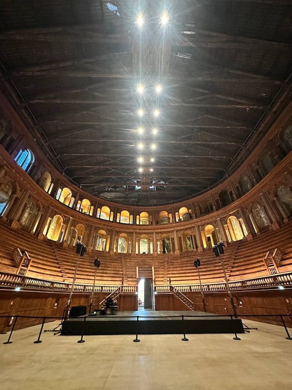 Da Vinci & Mutti: A Visit to Parma, Italy. 5 A grand historic theater in Parma with wooden tiered seating, ornate statues, and a high vaulted ceiling evokes the artistry of Da Vinci. Bright lights shine above, illuminating the elegant architectural details as viewed from the stage.