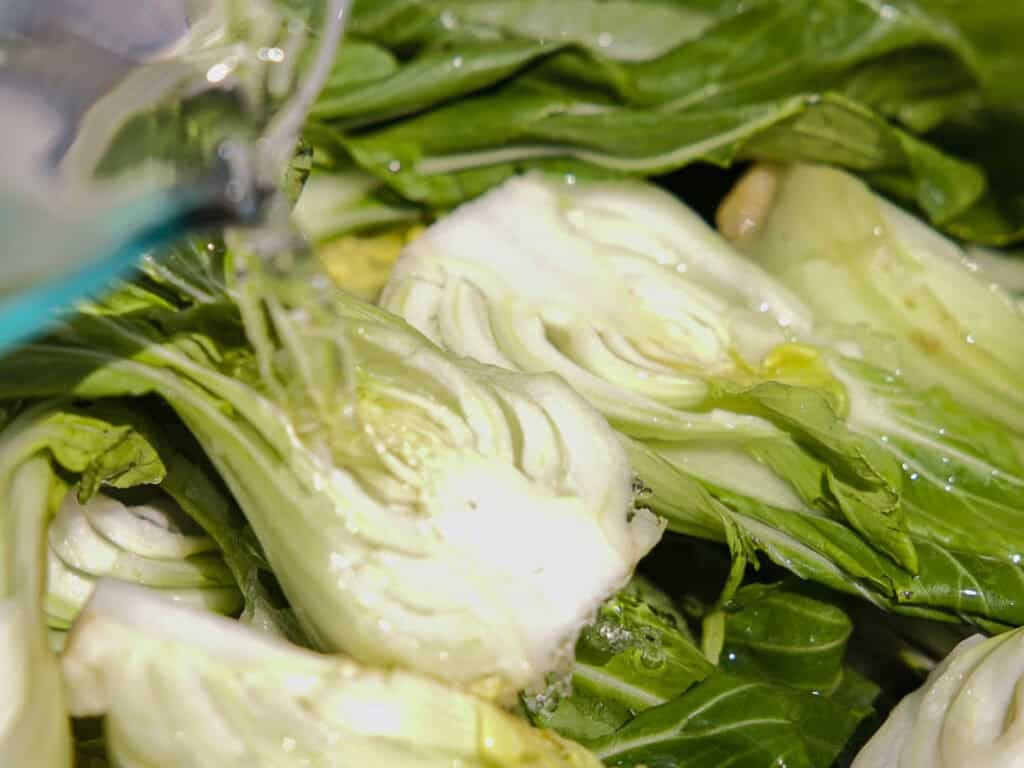 BEST Baby Bok Choy Kimchi Recipe - Easy & Delicious 25 Close-up of fresh bok choy being washed with running water, highlighting green leaves and white stemsโperfectly prepared for making homemade bok choy kimchi.