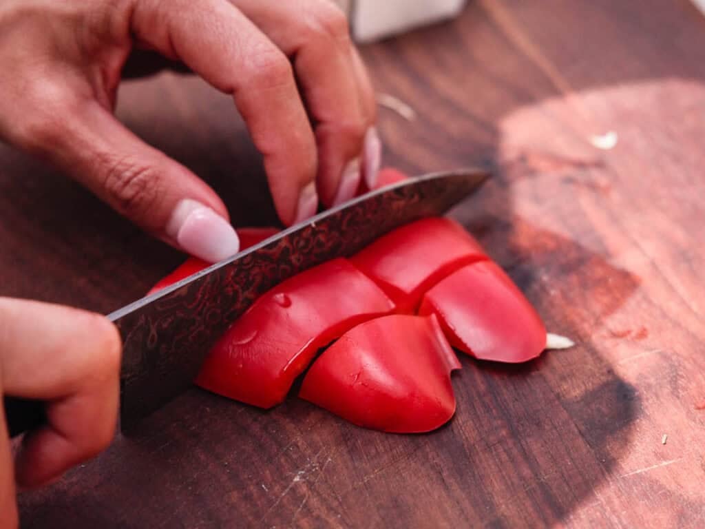 BEST Baby Bok Choy Kimchi Recipe - Easy & Delicious 14 A person slices a red bell pepper on a wooden cutting board with a knife, preparing fresh ingredients for homemade bok choy kimchi.
