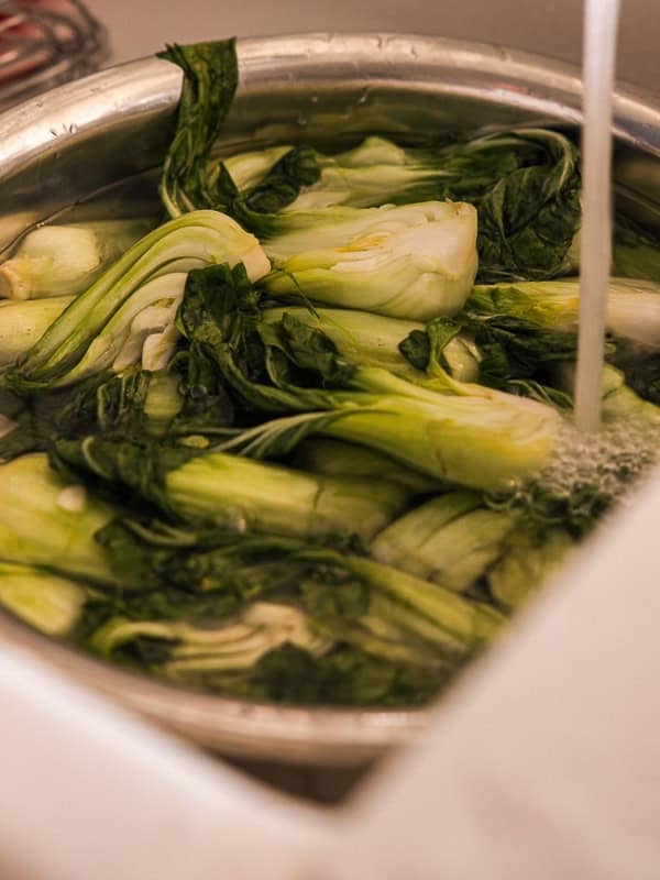 BEST Baby Bok Choy Kimchi Recipe - Easy & Delicious 36 Fresh bok choy, soon to be transformed into bok choy kimchi, soaked in a metal bowl of water in a kitchen sink, with a stream of water running into the bowl for washing.