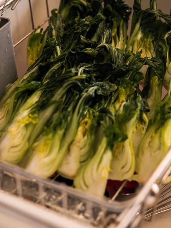 BEST Baby Bok Choy Kimchi Recipe - Easy & Delicious 37 Several halved heads of fresh leafy green vegetables, possibly escarole or romaine lettuceโand perhaps even some bok choy kimchiโare arranged in rows inside a metal tray or rack, ready for washing or drying.