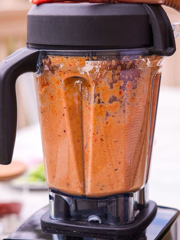 BEST Baby Bok Choy Kimchi Recipe - Easy & Delicious 34 A blender filled with a thick, orange-red bok choy kimchi sauce is being used, with someone's hand pressing on the top lid to keep it secure.