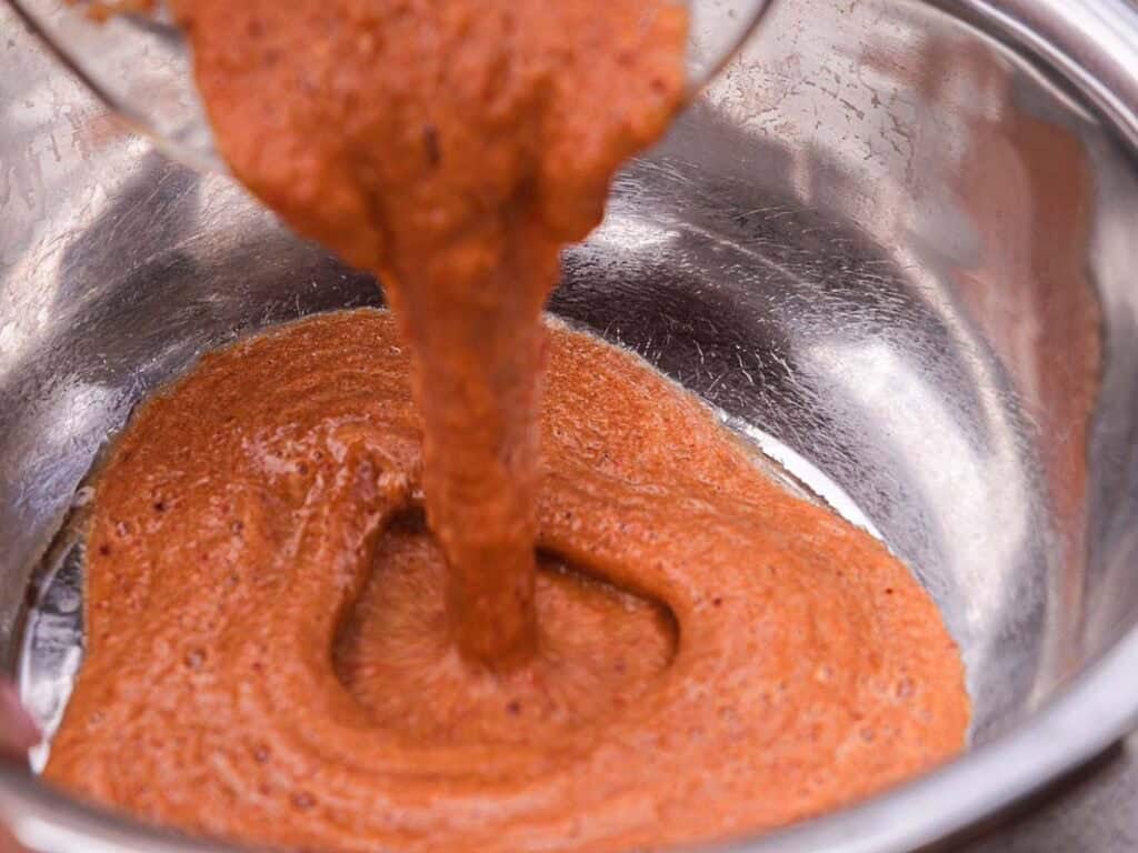 BEST Baby Bok Choy Kimchi Recipe - Easy & Delicious 38 A thick, reddish-brown batter, reminiscent of the bold hues found in bok choy kimchi, is being poured from a bowl into a larger metallic mixing bowl.